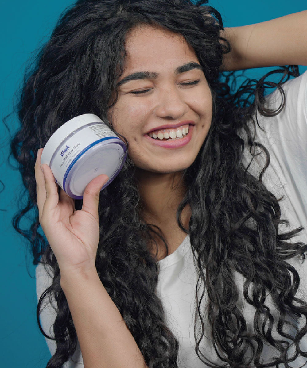 Smiling woman with curly hair holding Vilvah Goat Milk Hair Mask