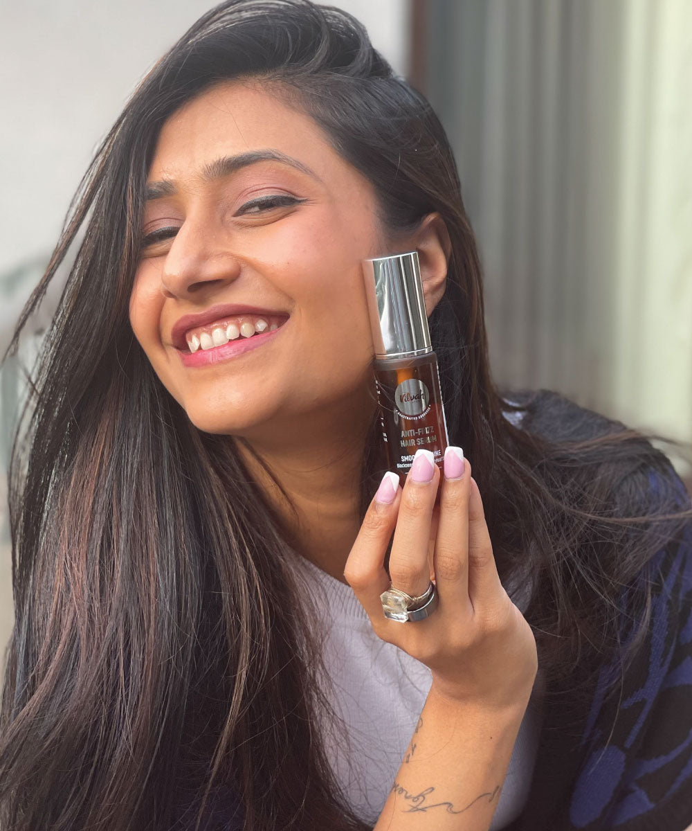 Smiling woman holding Vilvah Anti-Frizz Hair Serum for smooth, frizz-free hair care